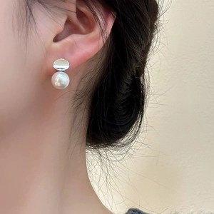 Close-up of elegant pearl earrings with silver disc detail worn by a model