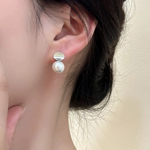 Detail of elegant white pearl earrings on ear with silver metal disc minimalist design