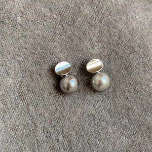 Elegant silver metallic pearl earrings on grey knit fabric background with soft lighting