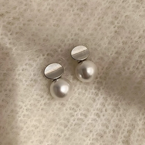 Detailed macro view of elegant pearl drop earrings against a soft knit sweater background
