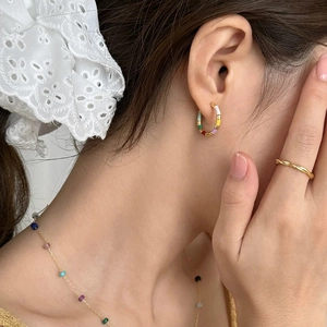 Close-up of French retro enamel earrings, twisted gold rings and colorful beaded necklace
