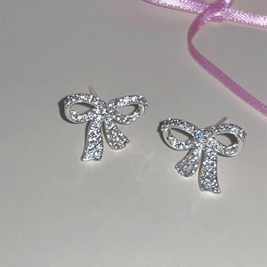 Détail des boucles d'oreilles nœud en argent avec pavé de zircons sur fond minimaliste