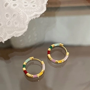 Detail of colorful enamel patchwork hoop earrings on a vintage brown mirror surface