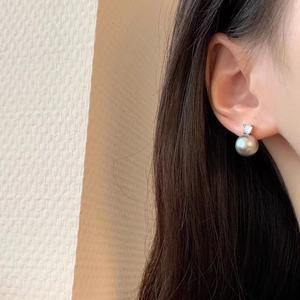 Close-up of elegant grey pearl stud earrings with sparkling zircon on earlobe