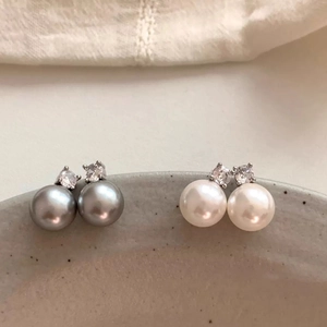 Elegant pair of grey and white pearl stud earrings with zircon inlay on a ceramic tray