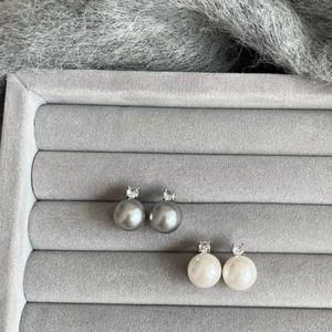 Detail of elegant white and grey pearl stud earrings with zircon stones on velvet tray