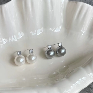 Macro shot of white and grey pearl earrings with zircons in a ceramic shell tray