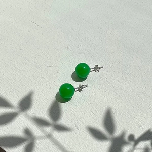 Detail of green chalcedony stud earrings on a textured surface with leaf shadows