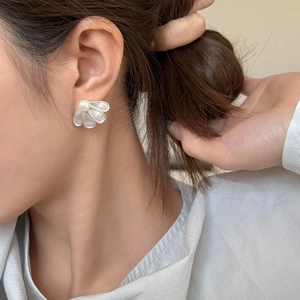 Detail of fan-shaped silver earring with white pearl and translucent petals on ear