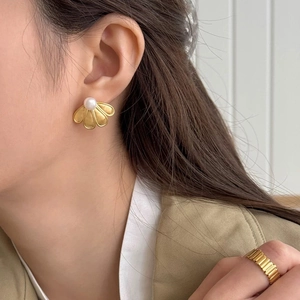 Detailed close-up of golden petal stud earring with pearl inlay worn by a model