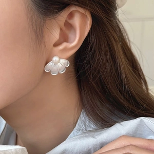 Detailed close-up of a fan-shaped silver stud earring with a white pearl on a model