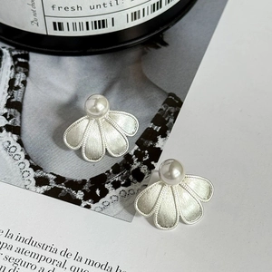 Macro detail of brushed silver flower earrings with white pearls on a magazine