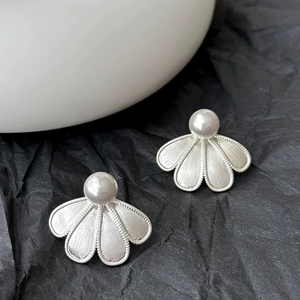 Detail of silver brushed petal earrings with white pearls on a textured black surface