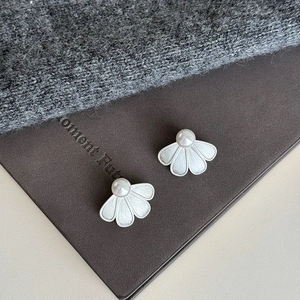 Detail of brushed metal petal earrings with elegant white pearl on a warm fabric background