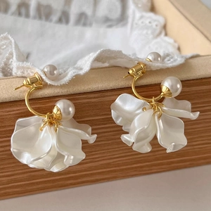Elegante Goldohrringe mit weißen Perlen und Blütenblättern über einer Schmuckschatulle