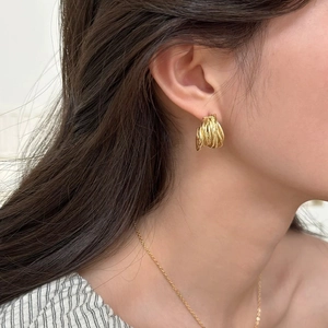 Détail de boucles d'oreilles dorées multicouches en forme de C portées par un mannequin