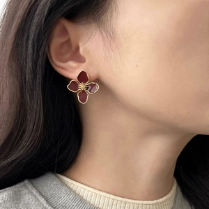 Close-up of a burgundy enamel flower earring with gold-tone accents worn by a model