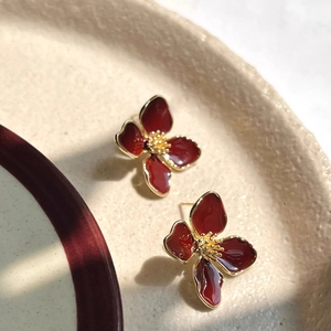 Detailed view of dark red enamel flower stud earrings with gold plating on ceramic