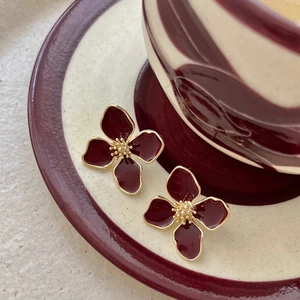 Detailed macro view of elegant burgundy enamel four-leaf flower earrings with gold finish