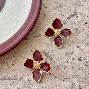 Detail of red enamel four-leaf flower earrings with golden bead centers on brown background