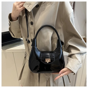 Detail of glossy black patent leather crescent bag with gold metal clasp and strap