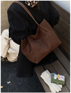 Detail of a brown suede tote bag on a wooden bench with winter accessories in warm lighting