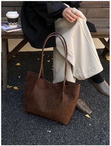 Close-up of deep brown suede tote bag on a wooden bench with autumn leaves