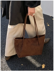 Detail of a large dark brown suede tote bag carried by a model on an autumn street