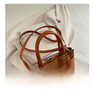 Gros plan sur le sac en daim marron avec anses en cuir orange et détail de boucle