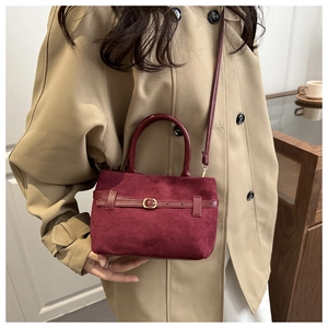 Gros plan du sac seau bordeaux en daim avec boucle dorée sur un trench-coat beige