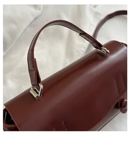 Detail of burgundy handbag with smooth leather texture and elegant silver metal handle buckle