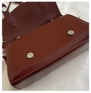 Close-up of a silver magnetic snap button on a dark brown leather flap square handbag