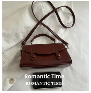 Detail view of small dark brown crossbody bag next to a phone for size comparison