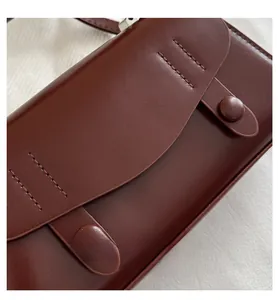 Detail of dark brown leather handbag with flap cover and stitching on beige fabric