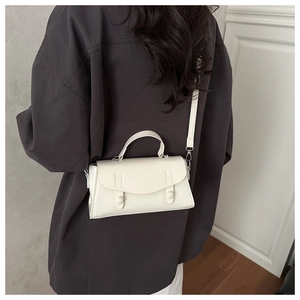 Close-up of minimalist white leather crossbody bag worn over a dark grey blazer jacket