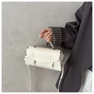 Chic white leather handbag with flap and cylindrical decorative buckles on grey wall