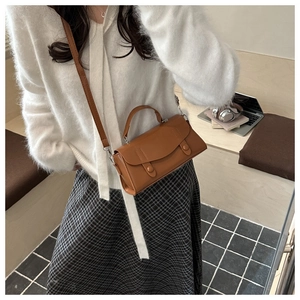 Detailed view of a brown faux leather crossbody bag worn by a model in a casual setting