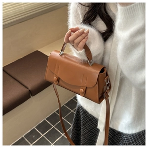 Close-up of caramel leather crossbody handbag with top handle and decorative stitching detail