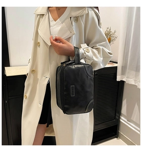 Close-up of black leather toiletry bag with dual zippers held by a model in a trench coat