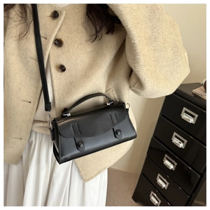 Detail of elegant black minimalist crossbody bag with top handle worn on a tweed jacket