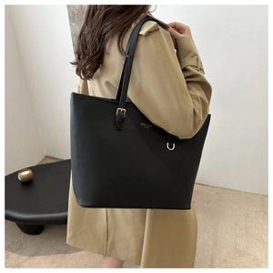 Dettaglio borsa tote nera in pelle minimalista indossata sopra un trench classico