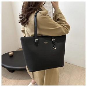 Dettaglio della borsa tote in pelle nera con logo dorato su un trench beige