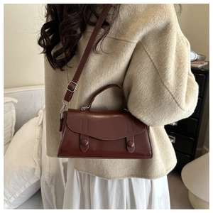 Detail of a dark brown leather crossbody bag with top handle and decorative buttons