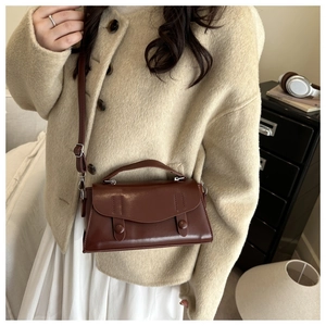 Brown leather crossbody bag paired with beige wool coat and white pleated skirt detail
