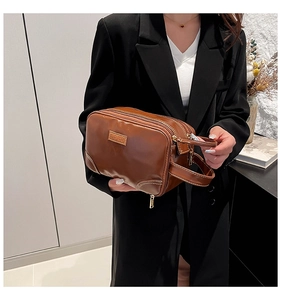 Brown leather pouch with multi-layer zippers and side handle shown in a lifestyle setting