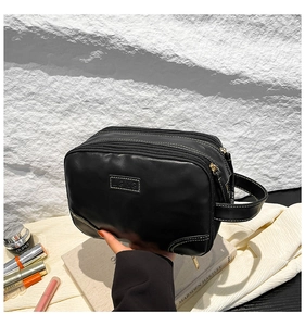 Detail of black multi-layer zipper cosmetic bag with premium leather texture and side handle
