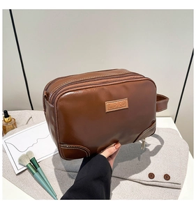 Detail of a brown PU leather toiletry bag featuring double zippers and a side handle strap