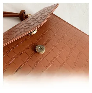 Detail view of brown crocodile texture handbag with brass magnetic buckle on white fabric