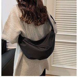 Detail of a black nylon crescent crossbody bag worn with a casual grey knit sweater