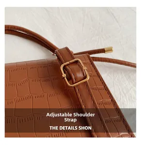 Detail of crocodile embossed leather bag featuring an adjustable gold-tone buckle strap
